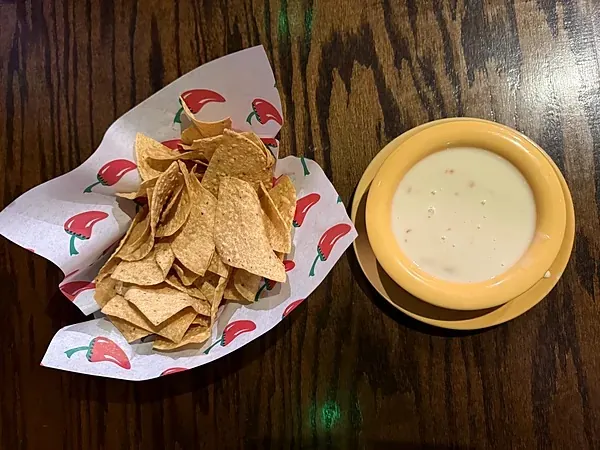 Tortilla chips in a chili pepper basket with a bowl of white queso at El Rancho