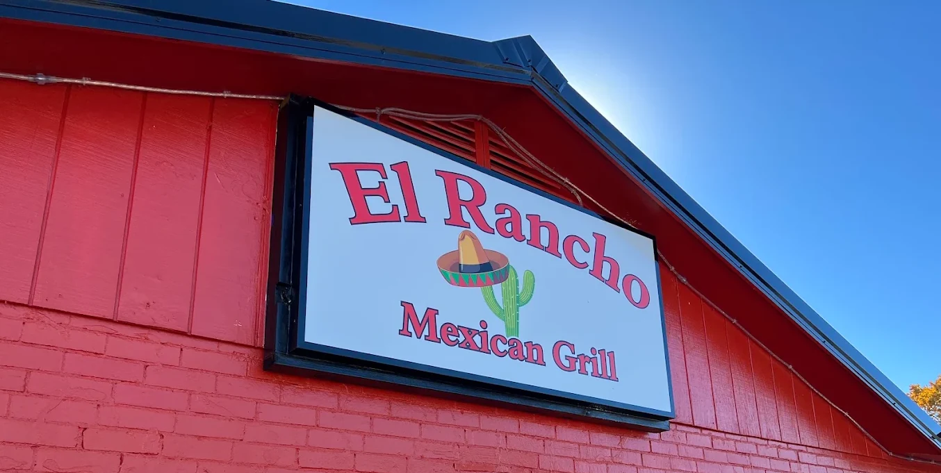 The red El Rancho Mexican Grill building with its sombrero-and-cactus sign and glowing OPEN window